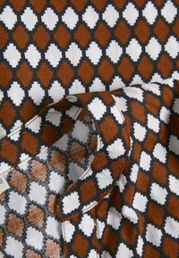 Tessuto multicolore caratterizzato da un motivo geometrico di diamanti marroni, bianchi e neri, con una texture liscia e dettagli di bordo piegato.