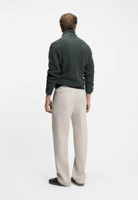 Mörkgrön ribbad stickad polotröja i kombination med ljusbeige byxor och svarta sneakers, sedd från baksidan.