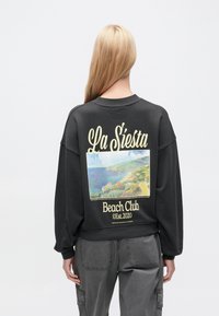 Μαύρο φούτερ με χαλαρή εφαρμογή, που διαθέτει πολύχρωμο γραφικό παραλίας και κείμενο "La Siesta Beach Club" στην πλάτη.