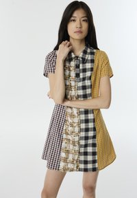 Vestido de manga corta y cuello que presenta un patchwork de varios patrones de cuadros en amarillo, negro, blanco y marrón, con un corte holgado.