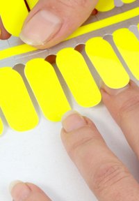 Fingers placing bright yellow adhesive nail strips on a flat surface, preparing for application.