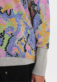 Färgglad stickad tröja med en blandning av rosa, blå, grön och orange mönster på en grå bas; ribbade manschetter; slät yta.