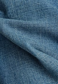 Tissu en denim bleu clair, présentant un tissage texturé avec une main douce. La surface affiche un motif uniforme de lignes en sergé.