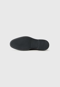Suela de zapato de goma negra con una superficie texturada y un tacón redondeado. Diseño simple, sin patrones ni acentos visibles.