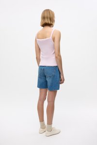 Hele roosa ilma käisteta topp ja pleekinud sinised denim lühikesed püksid. Lühikesed, sirged püksid on rebenenud äärega. Modell kannab beeži sokke ja valgeid kingi.