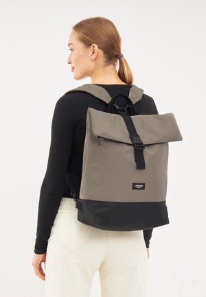 Backpack features a roll-top design in olive green and black, made of durable fabric with adjustable straps and a brand label on front.