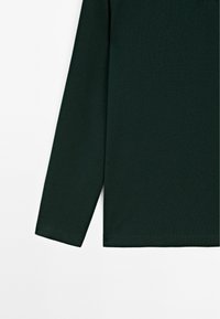 Donkergroene langemouwen shirt van textuurstof, met een rechte snit en zoom. Naaddetails zichtbaar langs de mouwen.