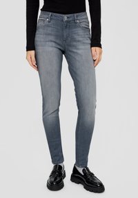 Vaqueros ajustados gris desgastado con diseño de cinco bolsillos, botón de metal y detalles de costura. Combinados con mocasines negros y una camiseta negra.