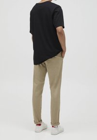 Svart bomullströja med rund hals, kombinerad med beige byxor. Vita sneakers med röda accenter. Avslappnad stil, enkel design.