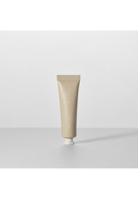 Beige kosmetisk tub med ribbad topp och platt botten, prydd med minimalistisk vit text. Slät yta, cylindrisk form, tätad munstycke.