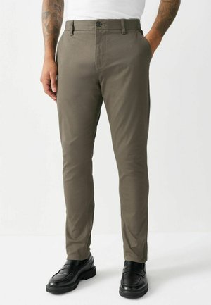 Olive green slim-fit chinos made from smooth fabric, featuring a button closure and side pockets; paired with black loafers.