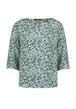 Blouse verte à motif floral blanc, col rond et manches trois-quarts.