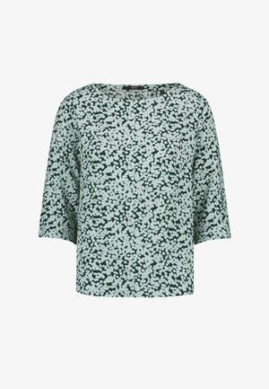 Blouse verte à motif floral blanc, col rond et manches trois-quarts.