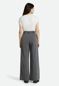 Parte superior blanca de manga corta y pantalones de pierna ancha grises de cintura alta, con un tejido texturizado y trabillas, vistos desde la espalda.