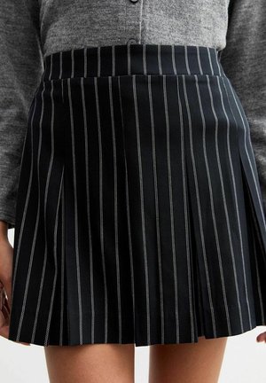 Jupe plissée noire à fines rayures blanches verticales, portée avec un cardigan gris boutonné, montrant une longueur mi-cuisse et une vue latérale des mains.