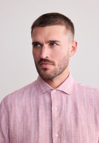 Rödrandig linneskjorta med uppvikt krage, korta ärmar och knäppning fram. Har ljusblå vertikala ränder och ett texturerat tyg.