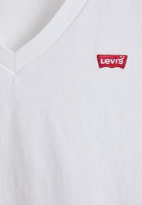 T-shirt en coton blanc à col en V avec un petit logo Levi's rouge brodé sur la poitrine côté gauche. Texture douce avec une coupe classique.