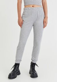 Graue Jogginghose mit elastischem Bund und schmal zulaufenden Knöcheln, kombiniert mit schwarzen Knöchelstiefeln mit dicker Sohle und Schnürdetails.