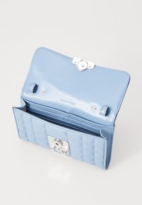Portofel din piele de culoare albastru deschis, cu un design matlasat, accesorii din argint și mai multe sloturi pentru carduri în interior. Dispune de o închidere tip snap și logo embosat.