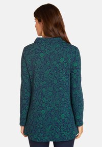 Grünes Blumenmuster auf einem dunkelblauen Hintergrund, langärmlige Tunika mit Kragen, glatte Textur und leicht abgerundeter Saum am unteren Ende.