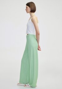 Lichtgroene, gestructureerde broek met wijde pijpen en hoge taille, gecombineerd met een witte crop top. De outfit heeft een ontspannen pasvorm en casual ontwerp.