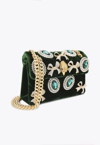 Groene fluwelen handtas versierd met een gouden ketting, grote turquoise edelstenen en zilveren accenten, met een strik en vissenmotieven.