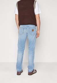 Vaqueros de mezclilla azul claro con un corte relajado, que cuentan con un parche de cuero de la marca en el bolsillo trasero y sutiles desgastes en las piernas.