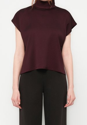 Bordowy krótki top z wysokim kołnierzem, krótkimi rękawami i gładką fakturą, zestawiony z czarnymi szerokimi spodniami.