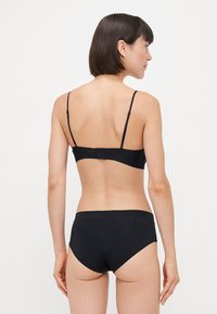 Ensemble bralette et bikini noir en tissu lisse. Le bralette présente des bretelles ajustables et une forme simple ; le bikini a une taille moyenne.