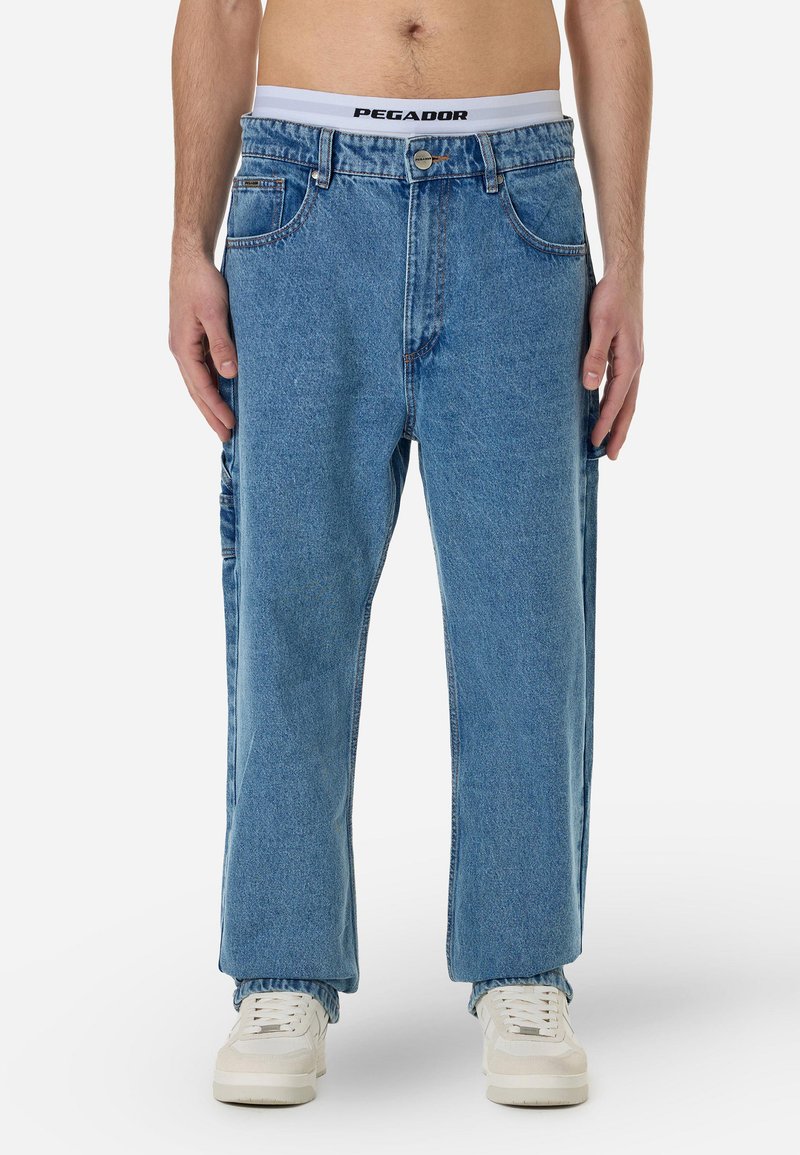 Kék farmernadrág, laza szabással, öt zsebes dizájnnal és gombos záródással. A dereka fehér, "PEGADOR" felirattal.