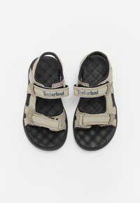 Bruine en zwarte sandalen met verstelbare banden, voorzien van een gestructureerde zwarte zool en "Timberland" merknaam op de banden.