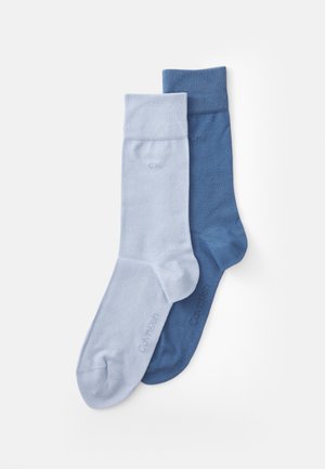 Kokvilnas maisījuma zeķes gaiši zilā un tumši zilā krāsā. Ar ribotām aprocēm un smalku zīmola logotipu. Mīksta tekstūra, standarta garuma dizains.