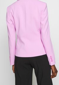 Růžový saka s úzkým střihem, jednolíný zadní rozparek a dlouhé rukávy s pěti knoflíky na každém manžetu.