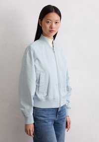 Jasnoniebieska kurtka bomberka z zamknięciem na zamek, ściągaczami na rękawach i luźnym krojem. Gładki materiał i boczne kieszenie dodają funkcjonalnych detali.