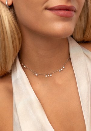 Silberne Choker-Halskette mit Tropfenakzenten, ausgestattet mit einer zarten Kette und polierter Oberfläche. Wird direkt über dem Schlüsselbein getragen.