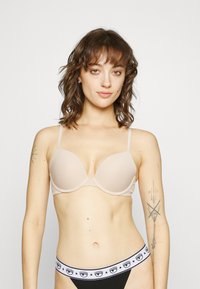 Sujetador acolchado beige con tirantes ajustables y diseño sin costuras. Tanga negro con una banda ancha que presenta un patrón de estrellas y motivos de pestañas.