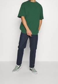 Grön bomull t-shirt, lös passform, rundad halsringning; matchad med mörkblå raka jeans. Skorna är gröna och vita med rutigt mönster.