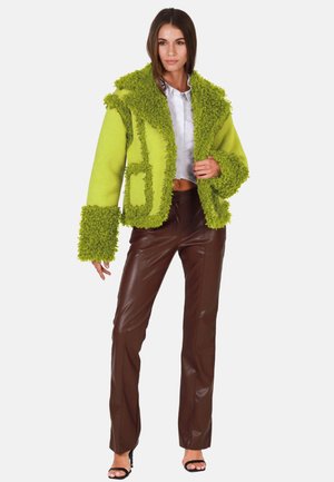 Grüne strukturierte Wolljacke mit flauschigem Besatz und weiten Ärmeln, kombiniert mit braunen, faux-ledernen Hose, die eine hohe Taille und schmale Passform hat.