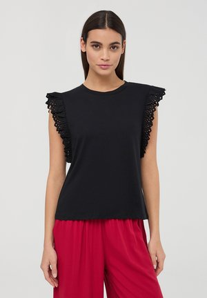 Top in cotone nero senza maniche con dettagli in pizzo arricciato sulle spalle. Presenta un colletto rotondo e una vestibilità ampia. Abbinato a pantaloni rossi a gamba larga.