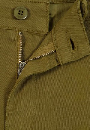 Close-up van kaki broek met gedeeltelijk open rits in zilverkleur en een knoop vastgemaakt boven de rits.