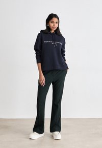 Námořnické mikina s kapucí s logem "TOMMY HILFIGER", spárovaná s tmavě zelenými širokými kalhotami a bílými platformovými teniskami. Hladká tkanina, uvolněný střih.