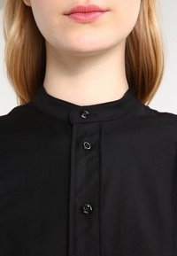 Czarna koszula z kołnierzykiem, charakteryzująca się gładką tekstur�ą, z okrągłymi czarnymi guzikami wzdłuż listwy oraz czystym, minimalistycznym wzornictwem.