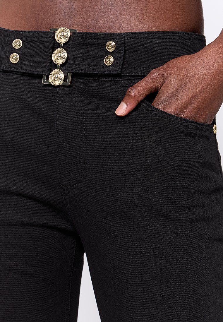 Czarne dżinsy o dopasowanym kroju, z zapięciem na złoty guzik i dwoma przednimi kieszeniami, prezentujące teksturowany materiał.