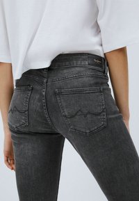 Grå denimjeans med enkla bakfickor som har ett vågigt sömnads mönster. Hög midja med en svart tygetikett vid midjebandet.