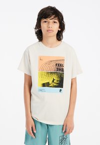Camiseta de manga corta color crema con un estampado gráfico que incluye elementos en naranja, amarillo y negro, representando a un surfista y patrones geométricos.