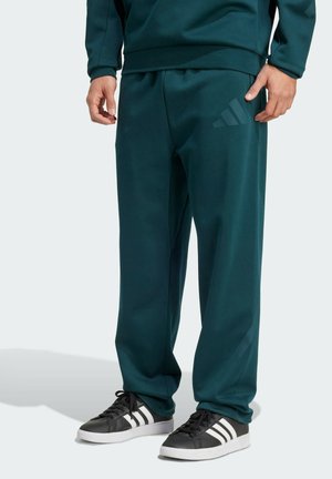 Teal sportbroeken van zachte stof, met een elastische tailleband en drie witte strepen op zwarte sportschoenen. Subtiele logodetail op het been.