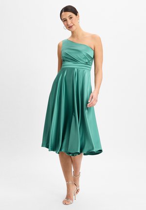 Vestito verde in raso a spalla unica con corpino aderente e gonna svasata, caratterizzato da arricciature in vita e una finitura liscia e lucida. Tacchi a strappo argentati.