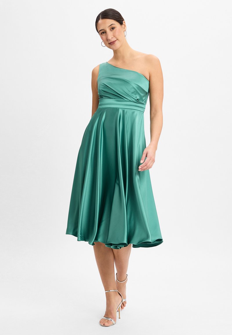 Satin, groen een-schouder jurk met een getailleerde bovenkant en een uitlopende rok, met rimpelingen in de taille en een gladde, glanzende afwerking. Zilveren strappy hakken.