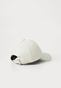 Weißer verstellbarer Baseballcap, auf der Seite liegend vor einem weißen Hintergrund, zeigt den hinteren Riemen und die Metallschließe.
