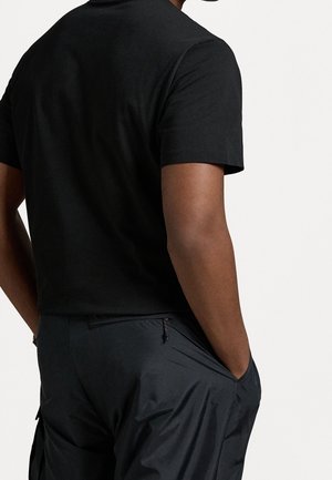 Czarny t-shirt z krótkim rękawem o gładkiej fakturze, zestawiony z ciemnymi spodniami cargo z bocznymi kieszeniami i suwakiem w okolicy talii.